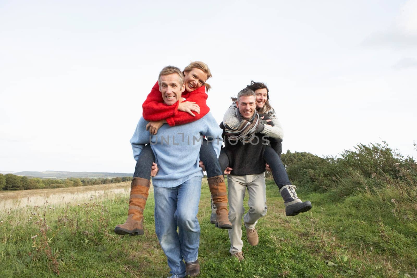 Two Couples Having Piggyback Ride In Autumn Landscape