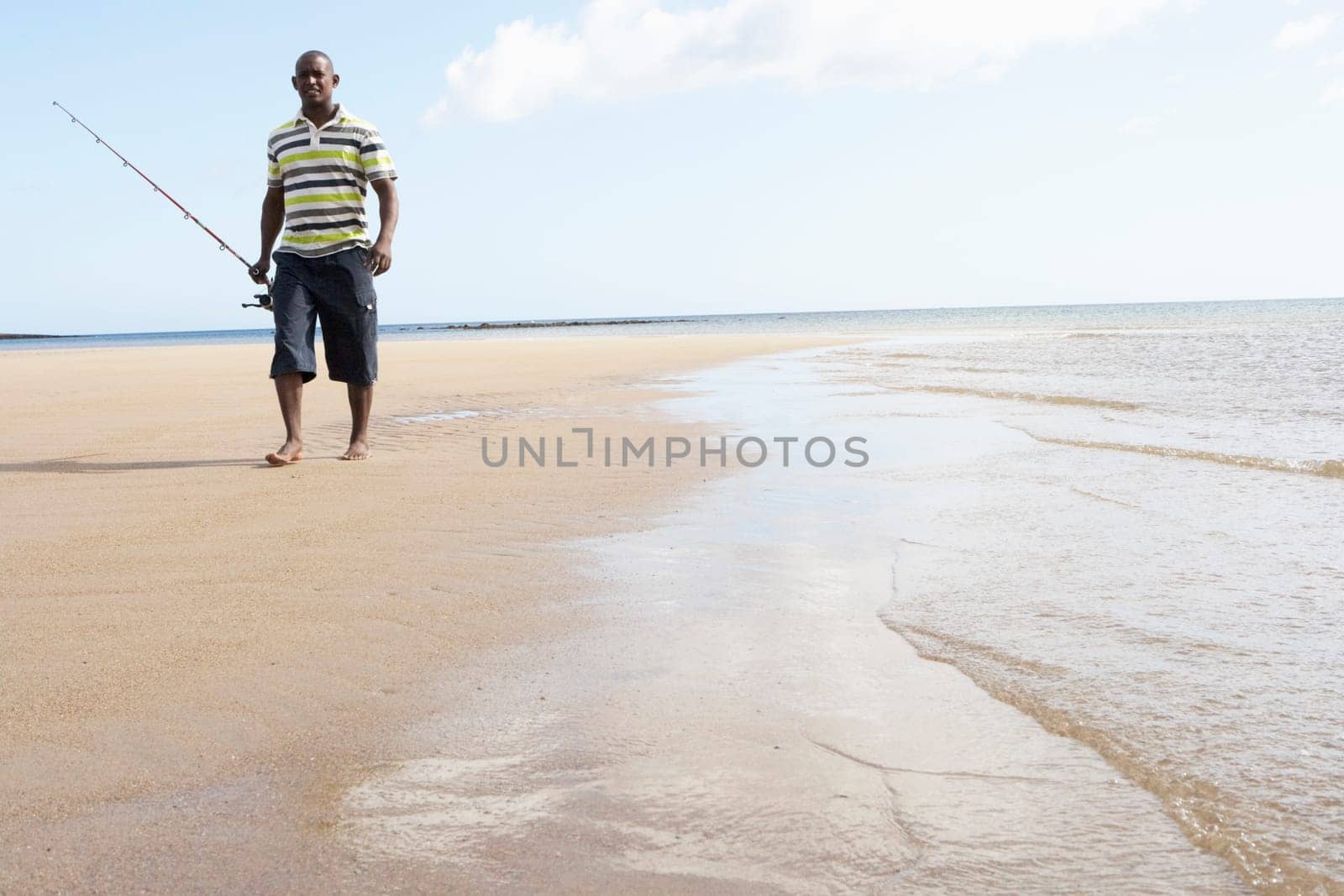 Man Walking Along Shore Of Beach Carrying Fishing Rod