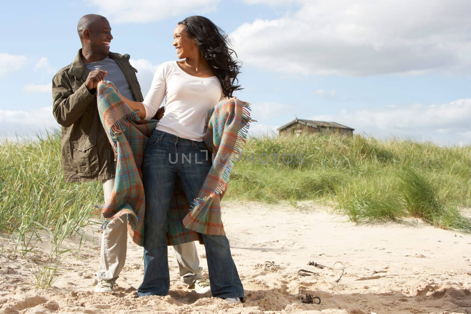 Romantic Young Couple Standing By Dunes With Beach Hut In Distance