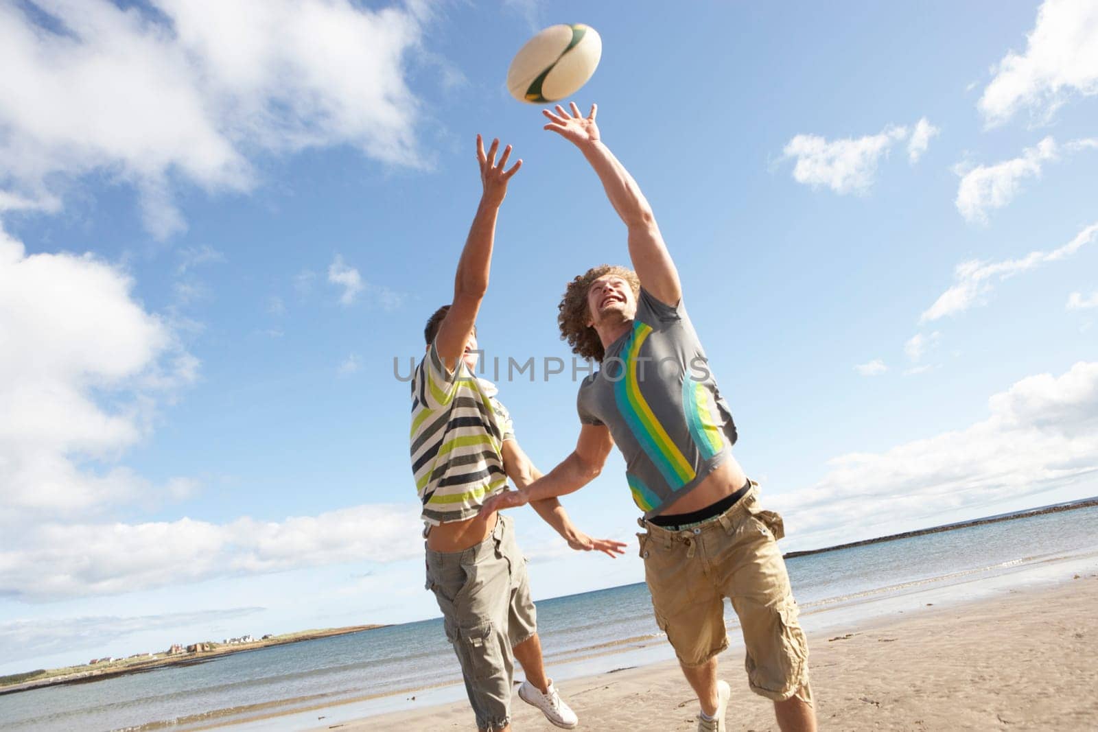 Two Teenage Boys Playing Rugby On Beach Together