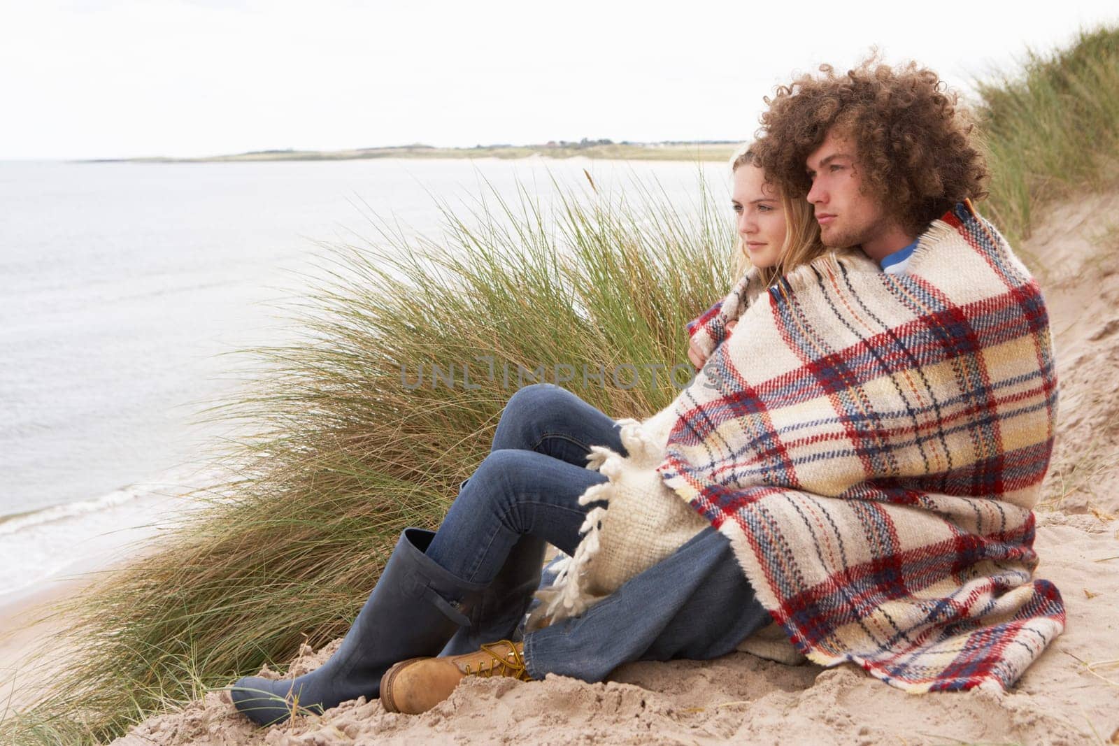 Teenage Couple Sitting In Sand Dunes Wrapped In Blanket