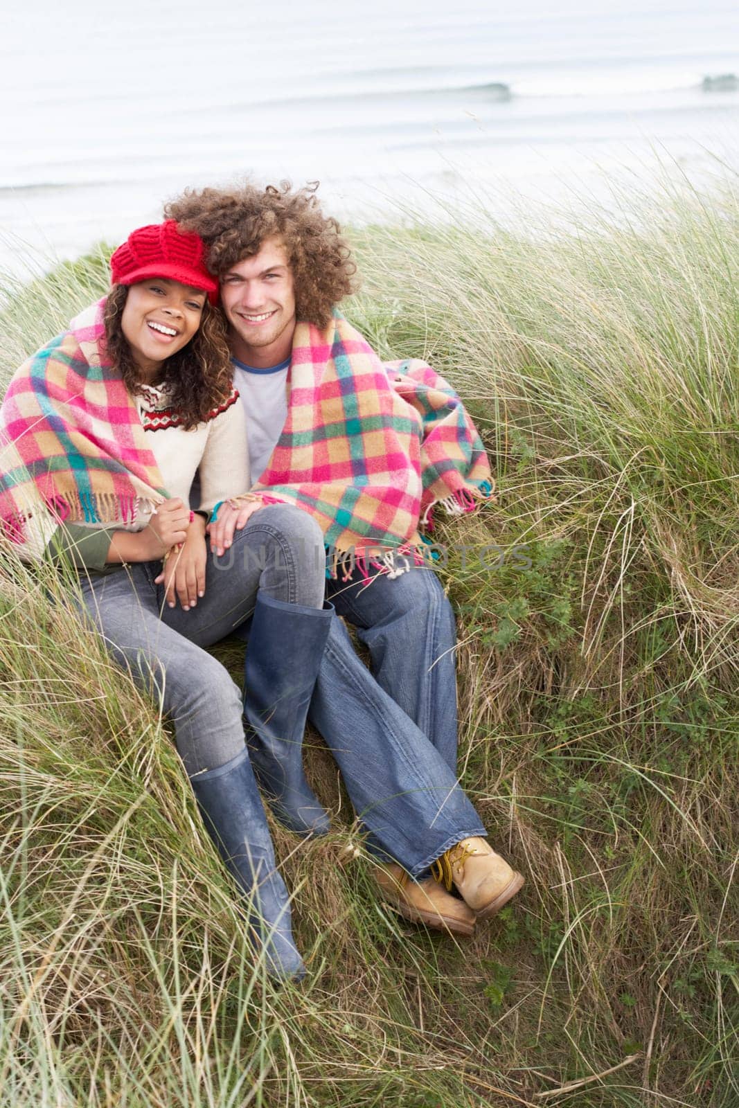 Young Couple Sitting In Sand Dunes Wrapped In Blanket