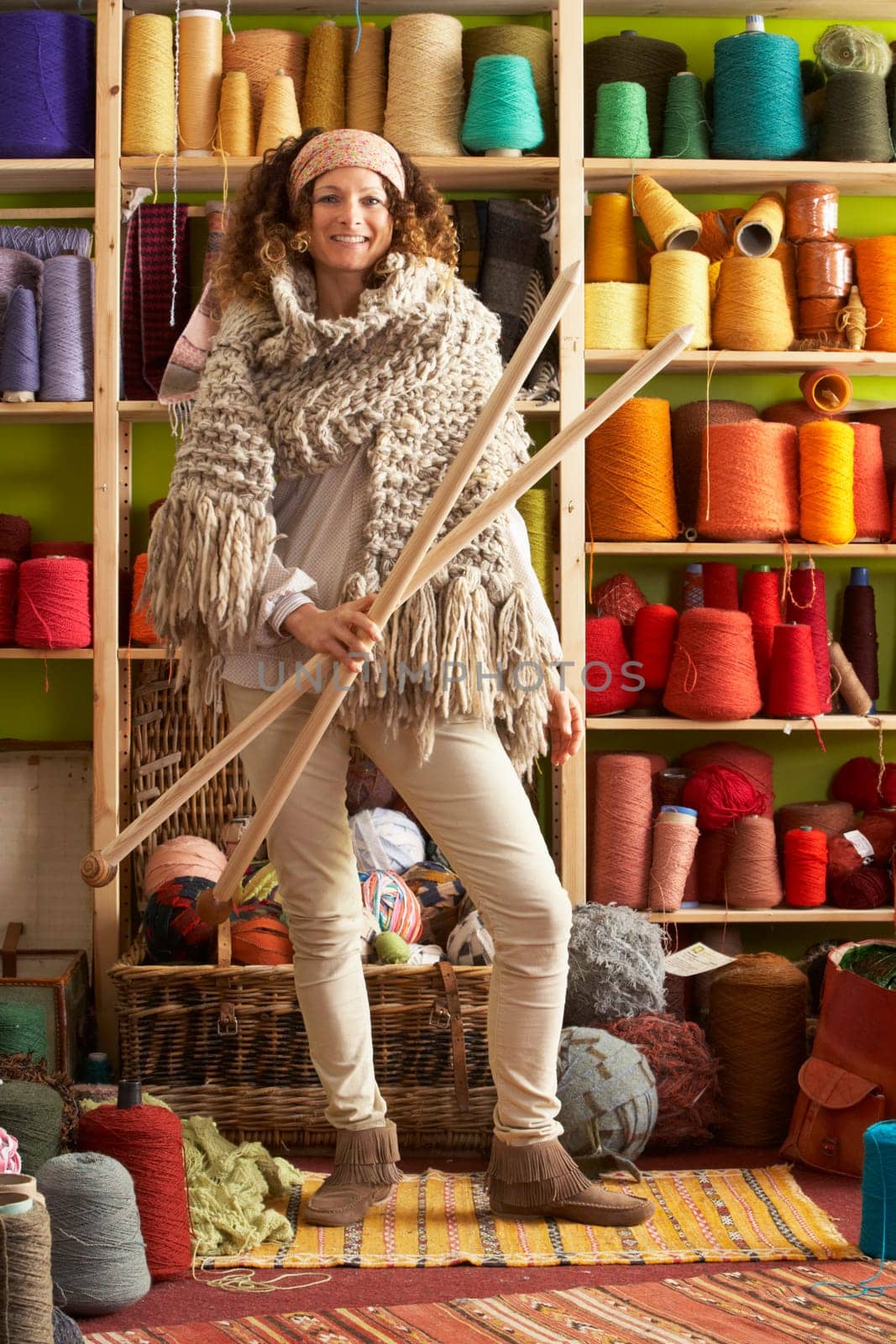Woman Wearing Knitted Scarf Standing In Front Of Yarn Display Holding Giant Needles