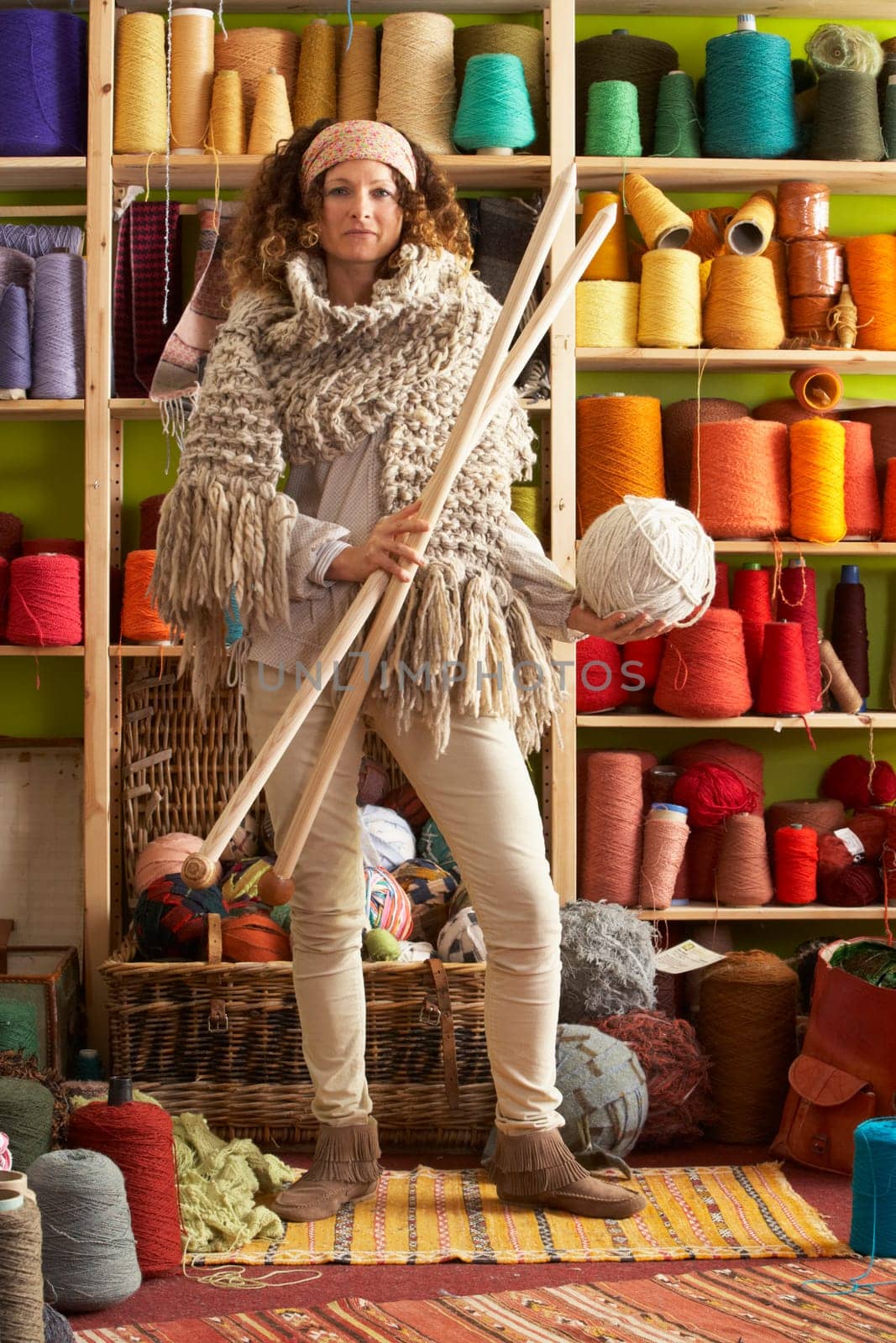 Woman Wearing Knitted Scarf Standing In Front Of Yarn Display Holding Giant Needles