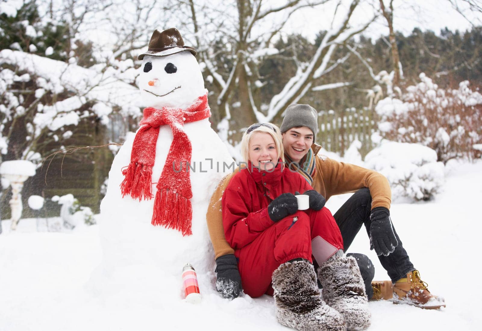 Teenage Couple In Winter Landscape Next To Snowman With Flask And Hot Drink