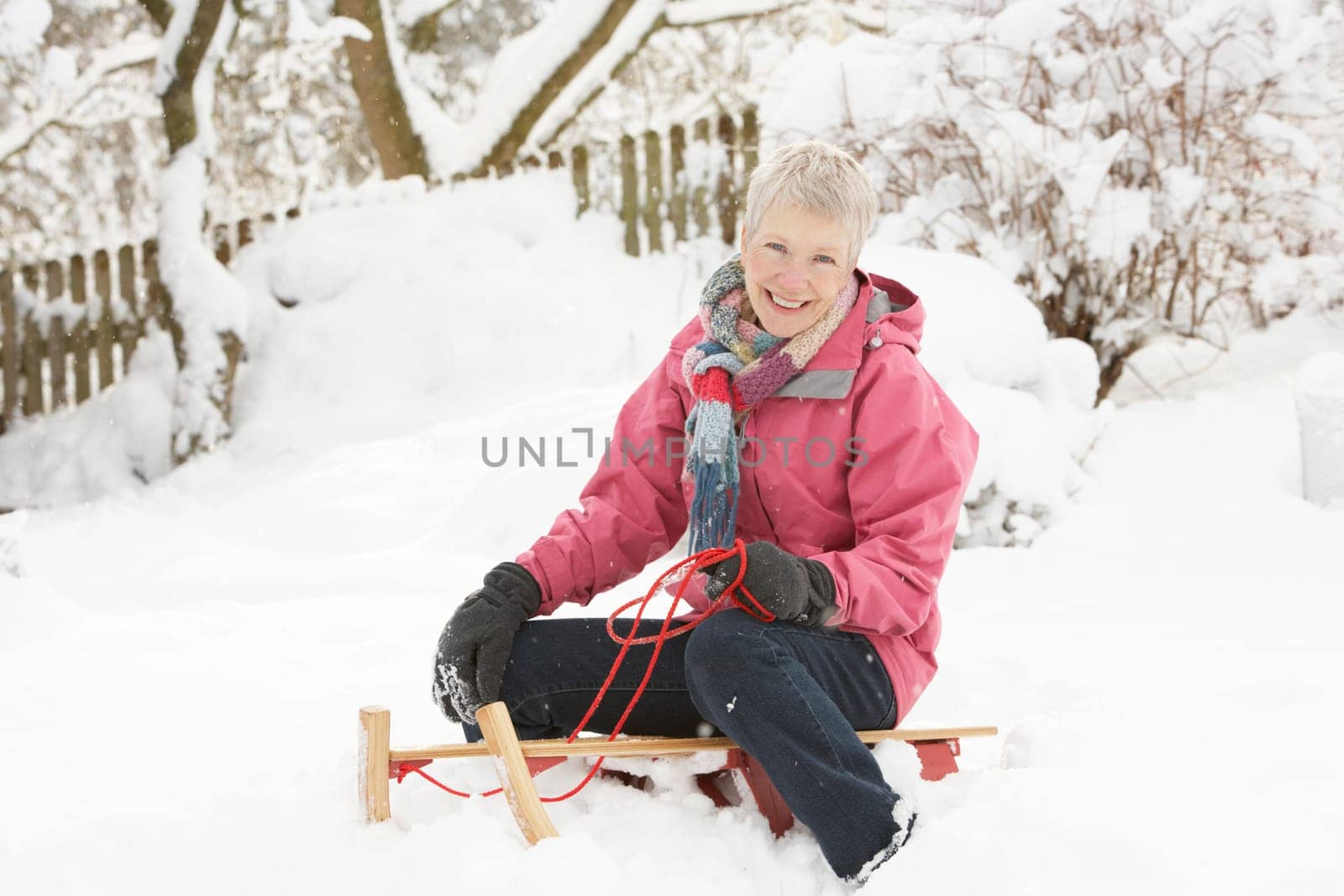 Senior Woman Sitting On Sledge In Snowy Landscape