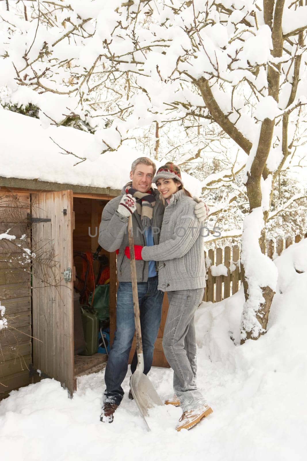 Young Couple Clearing Snow From Path To Wooden Store