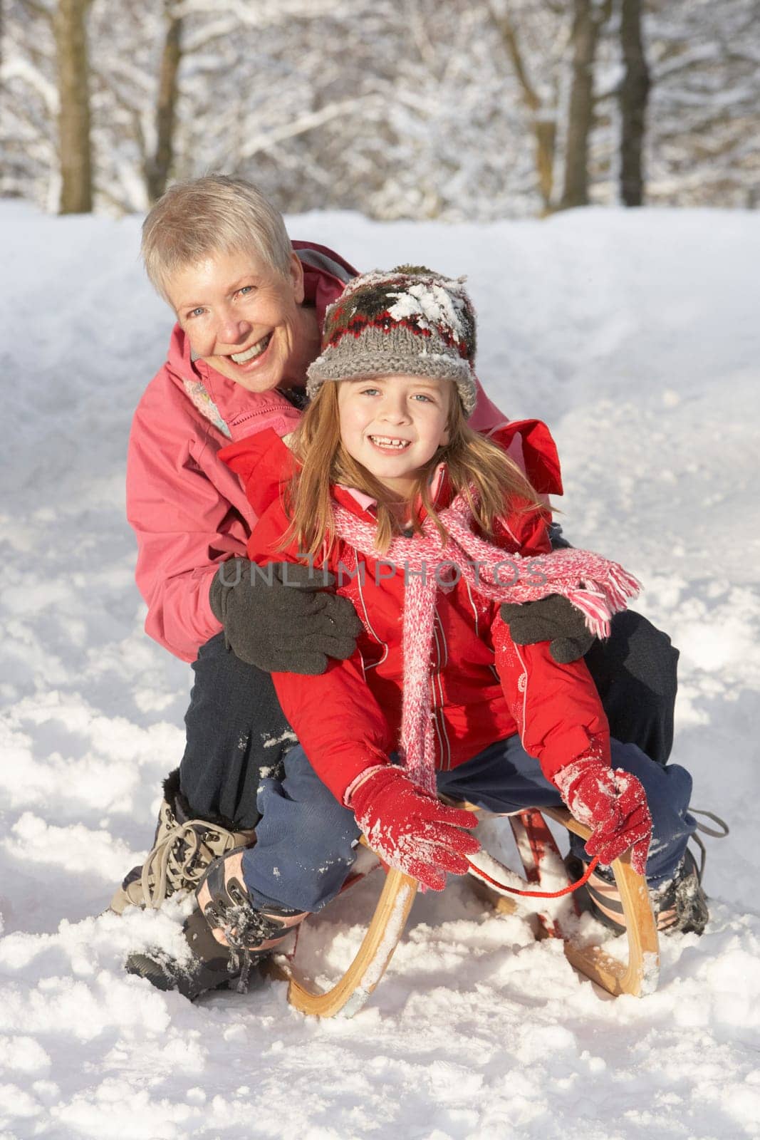 Young Girl With Grandmother Riding On Sledge In Snowy Landscape