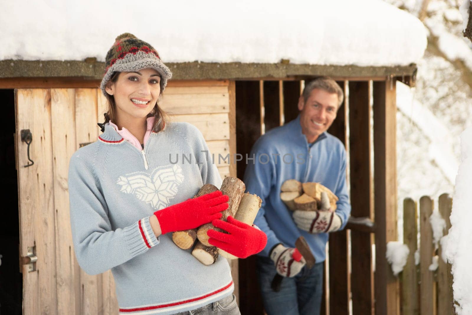 Young Couple Collecting Logs From Wooden Store In Snow