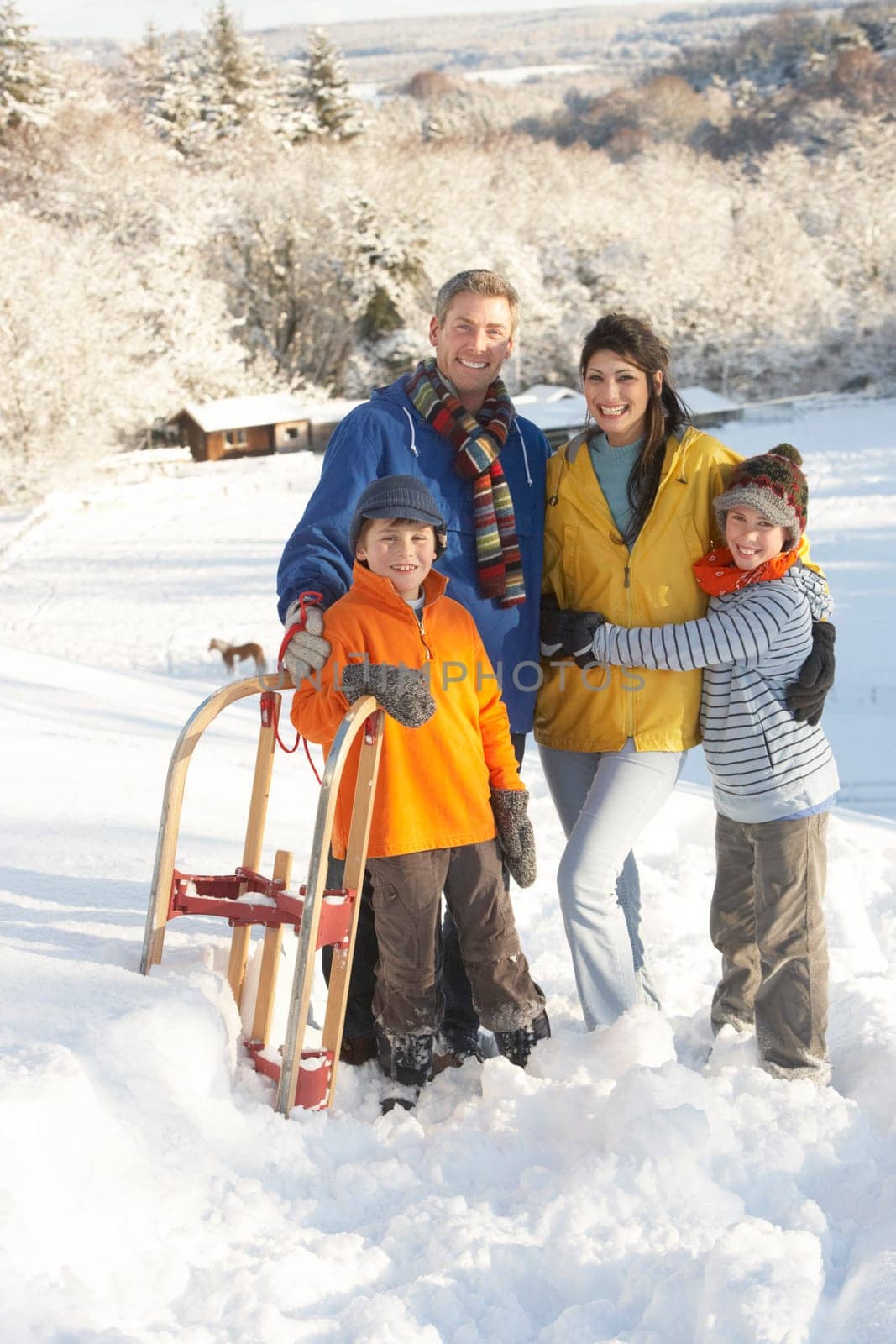 Young Family Standing In Snowy Landscape Holding Sledge