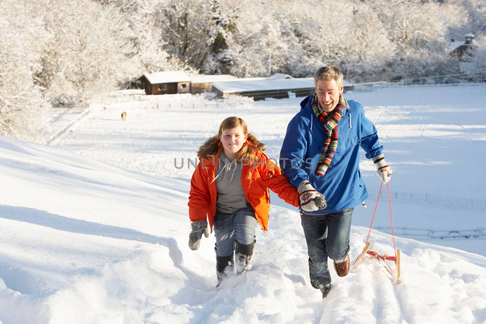 Father And Son Pulling Sledge Up Snowy Hill