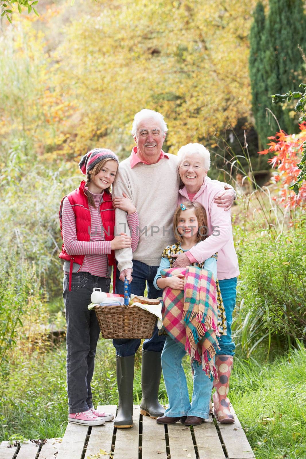 Grandparents With Grandchildren Carrying Picnic Basket By Autumn Woodland