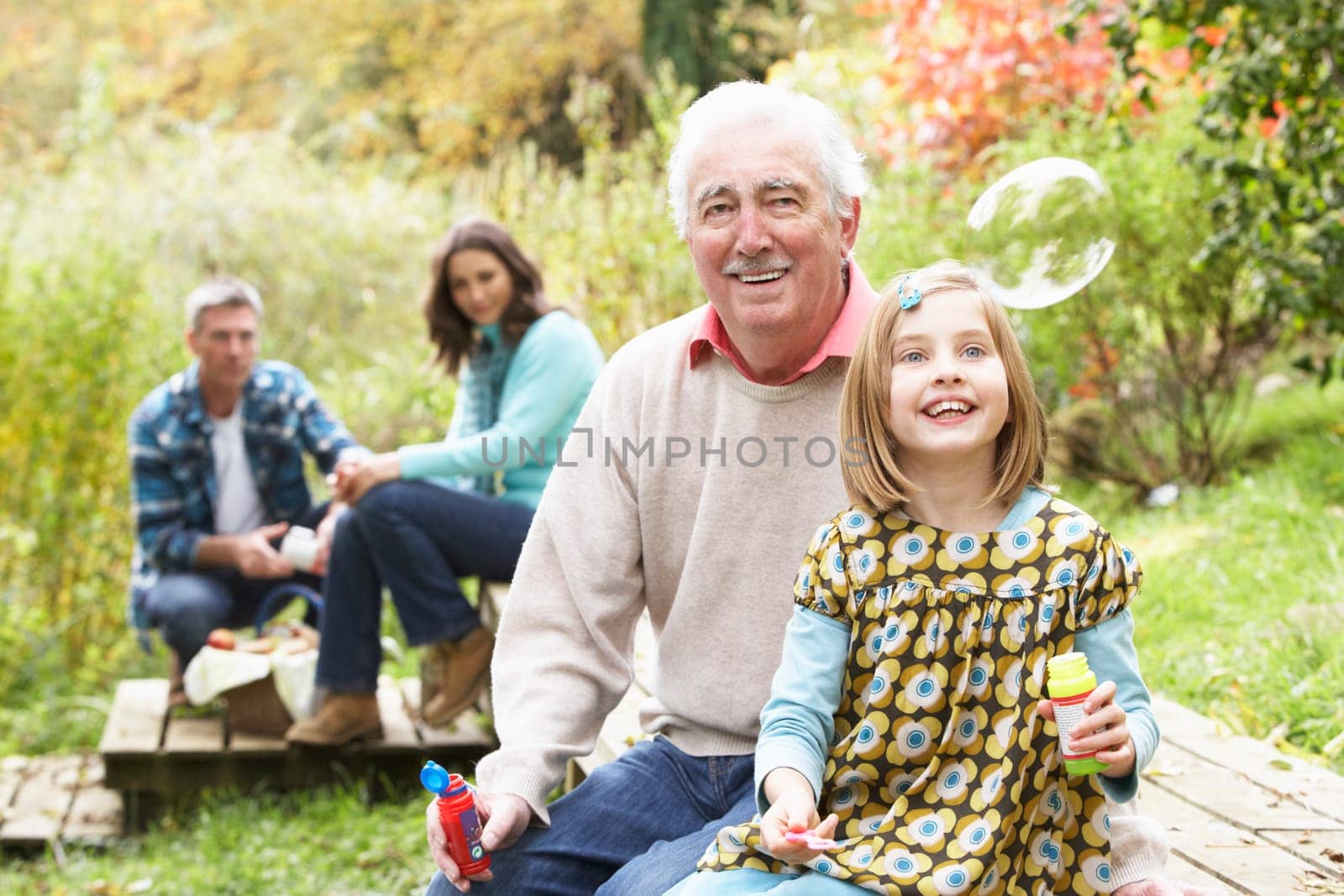 Grandfather And Granddaughter Blowing Bubbles On Family Picnic