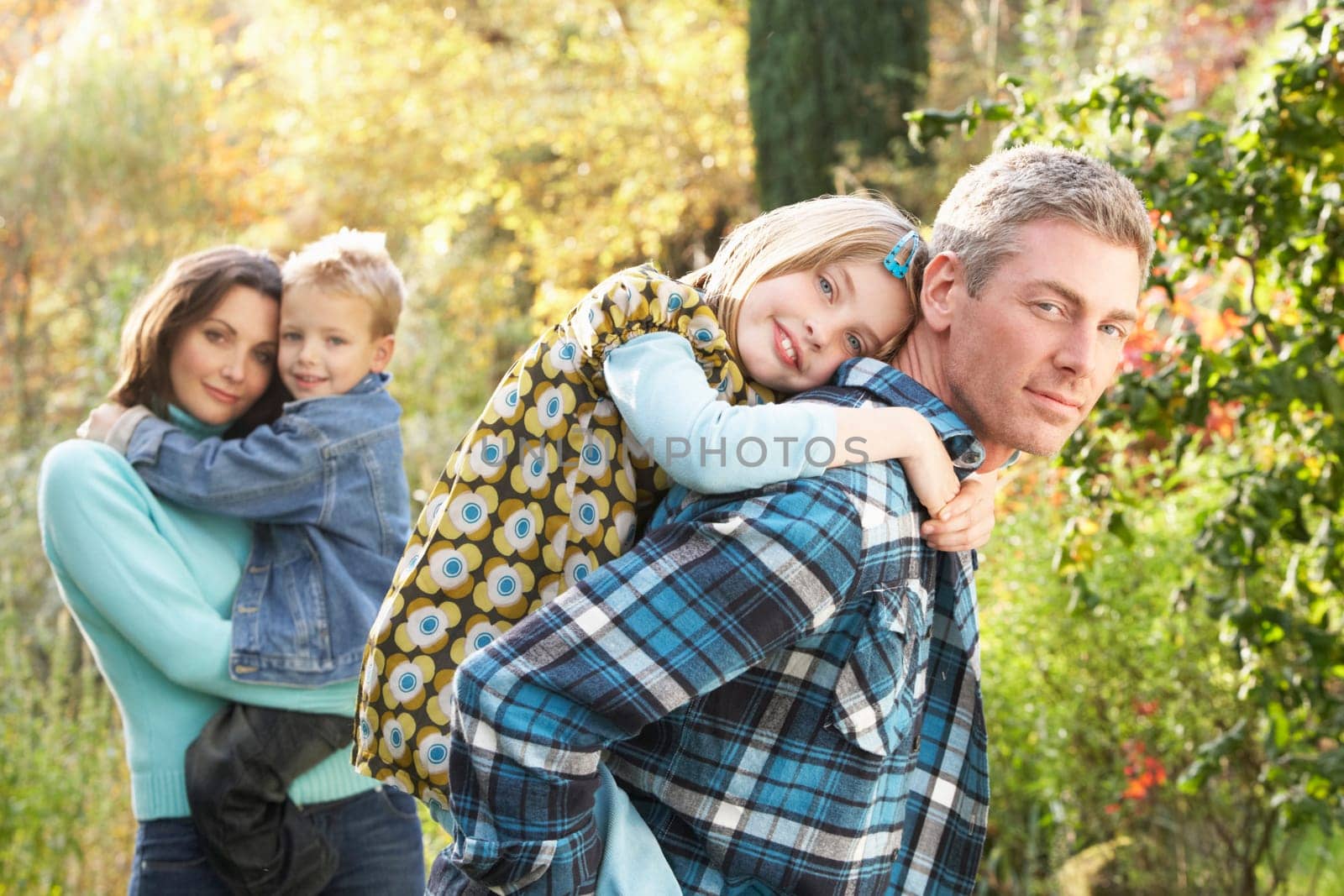 Family Group Outdoors In Autumn Landscape With Parents Giving Chiildren Piggybac