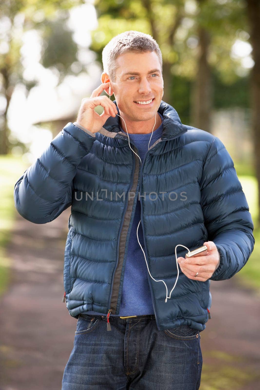 Man Listening To MP3 Whilst Walking In Autumn Park
