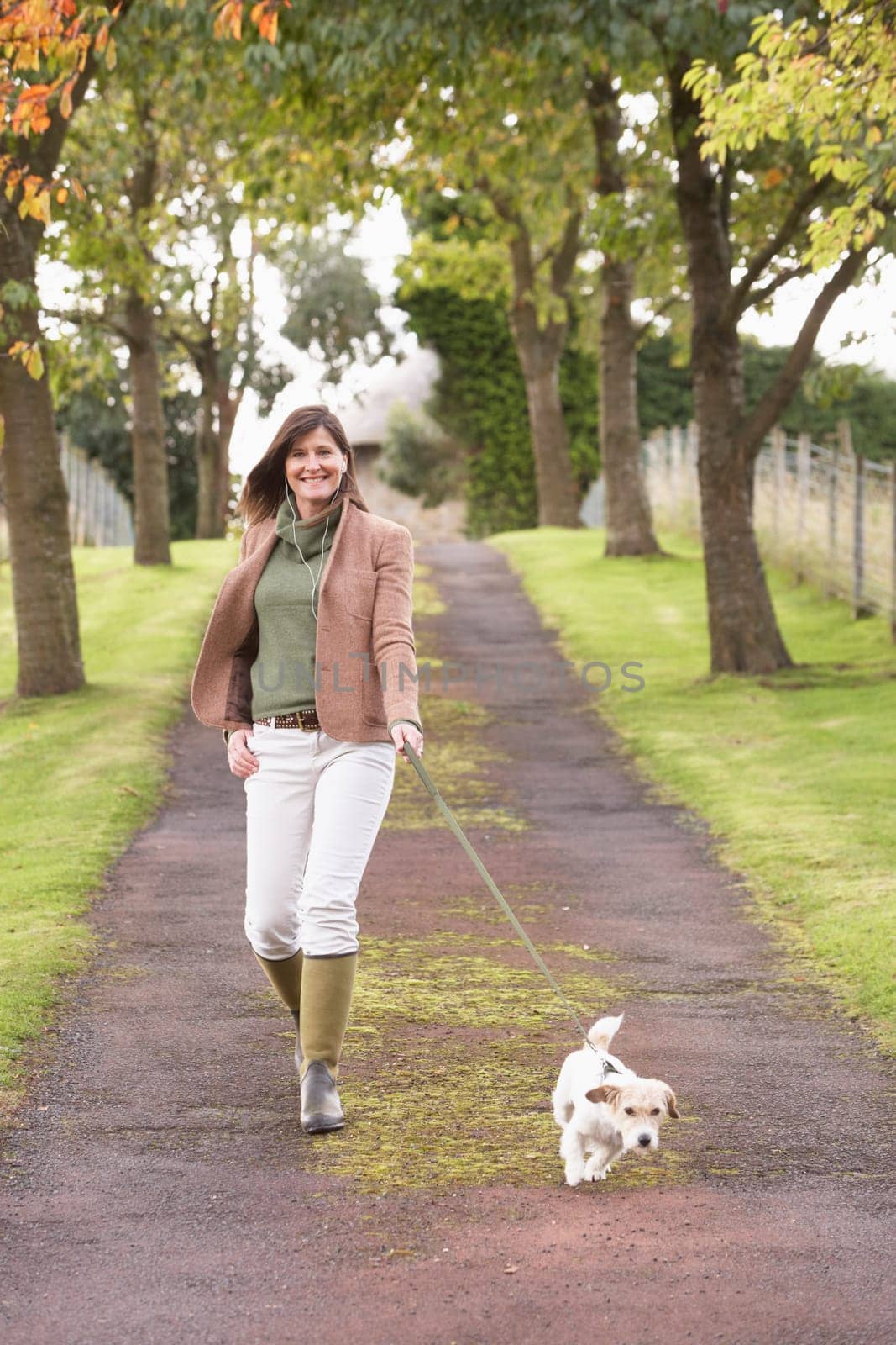 Woman Taking Dog For Walk Outdoors In Autumn Park