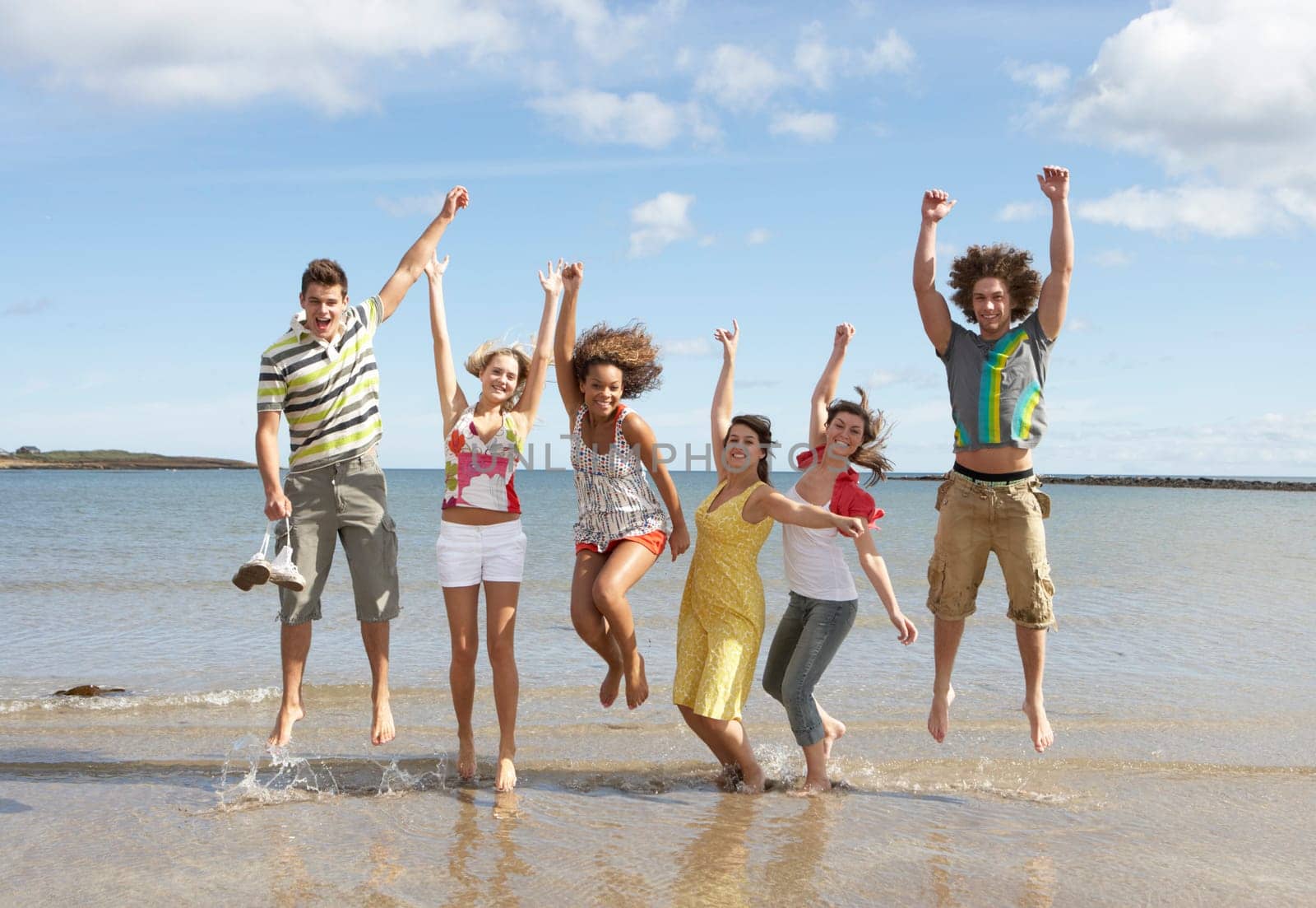 Group Of Teenage Friends Having Fun On Beach Together Jumping In Air
