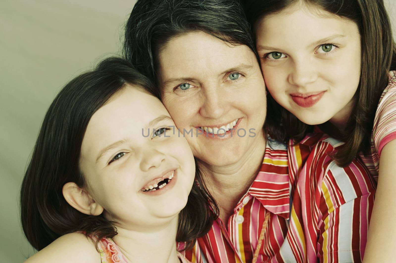 A mother and her two young daughters embrace and smile towards the camera. Horizontal shot