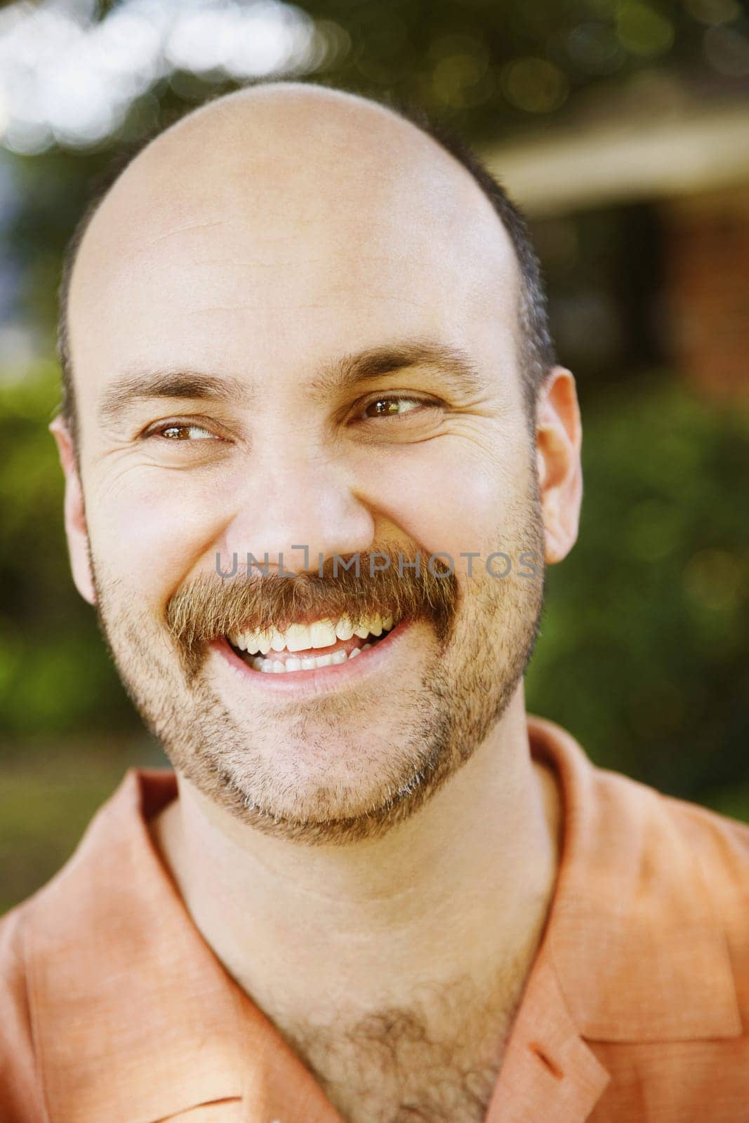 A handsome man with facial hair is smiling and looking off to the side. Vertical shot.