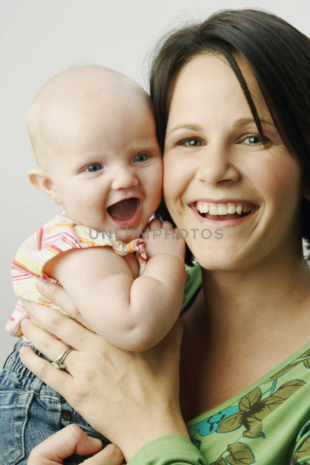 A mother is holding up her infant daughter and both are smiling for the camera. Vertical shot.