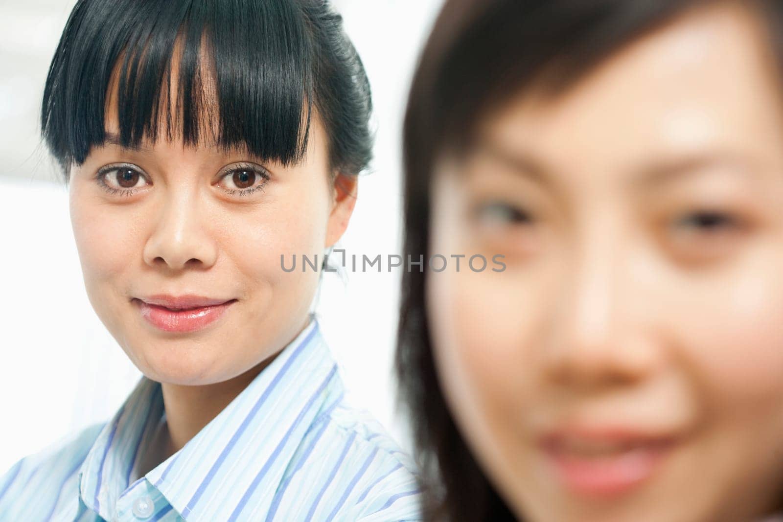 Two women smiling at the camera with the foreground woman out of focus. Horizontal shot.