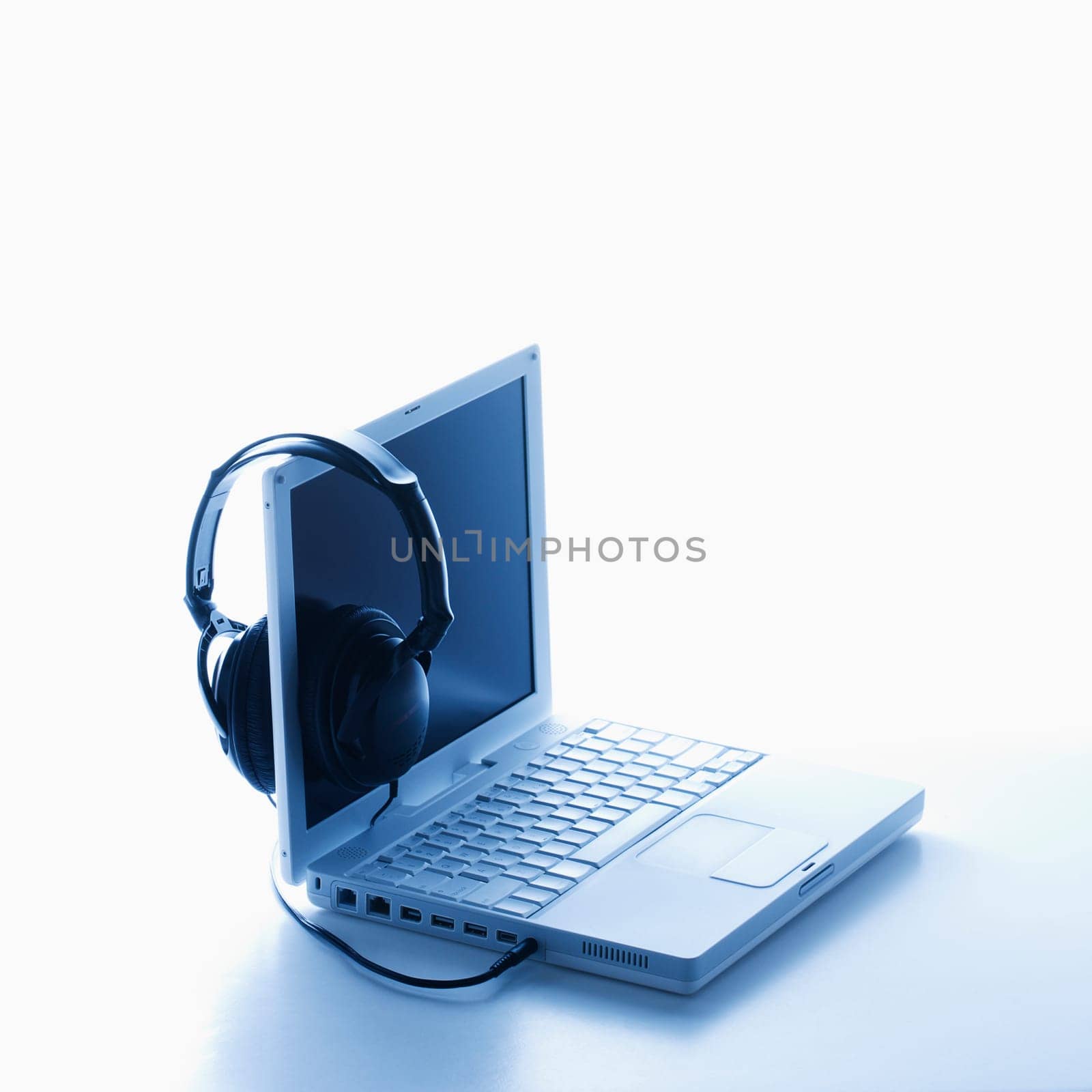 A pair of black headphones connected to a laptop and hanging on the screen. Square format. Isolated on white.