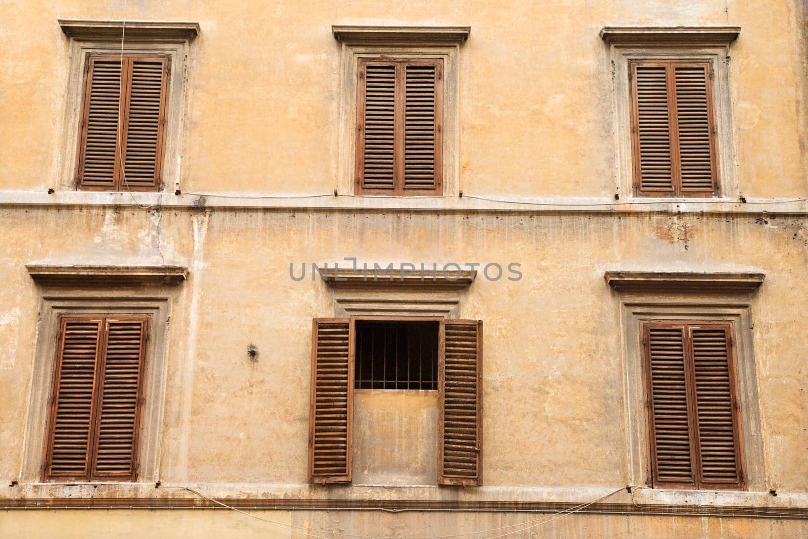 Shuttered windows in an old building, with the shutters closed on all windows but one. Horizontal shot.
