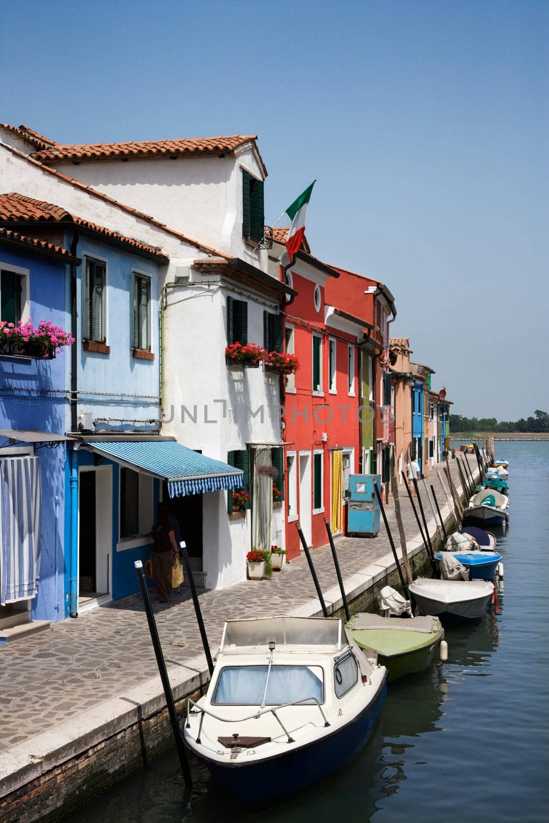 Buildings and docked boats on a canal in Venice, Italy, under blue sky. Vertical shot.