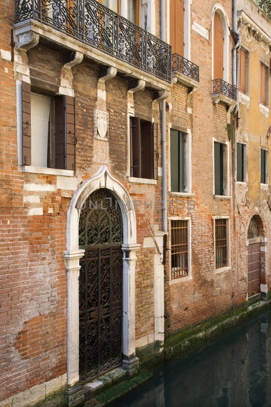 Canal leading up to ornate door gate of Venetian home. Vertical shot.