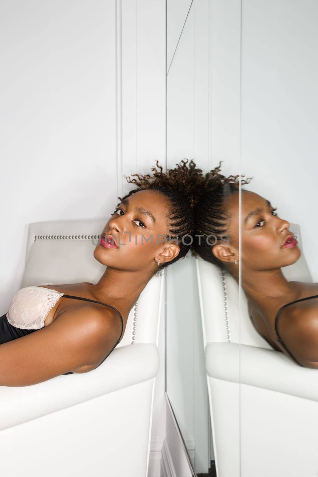 Attractive young woman reclining in a white chair with a mirror behind her head. Vertical shot.