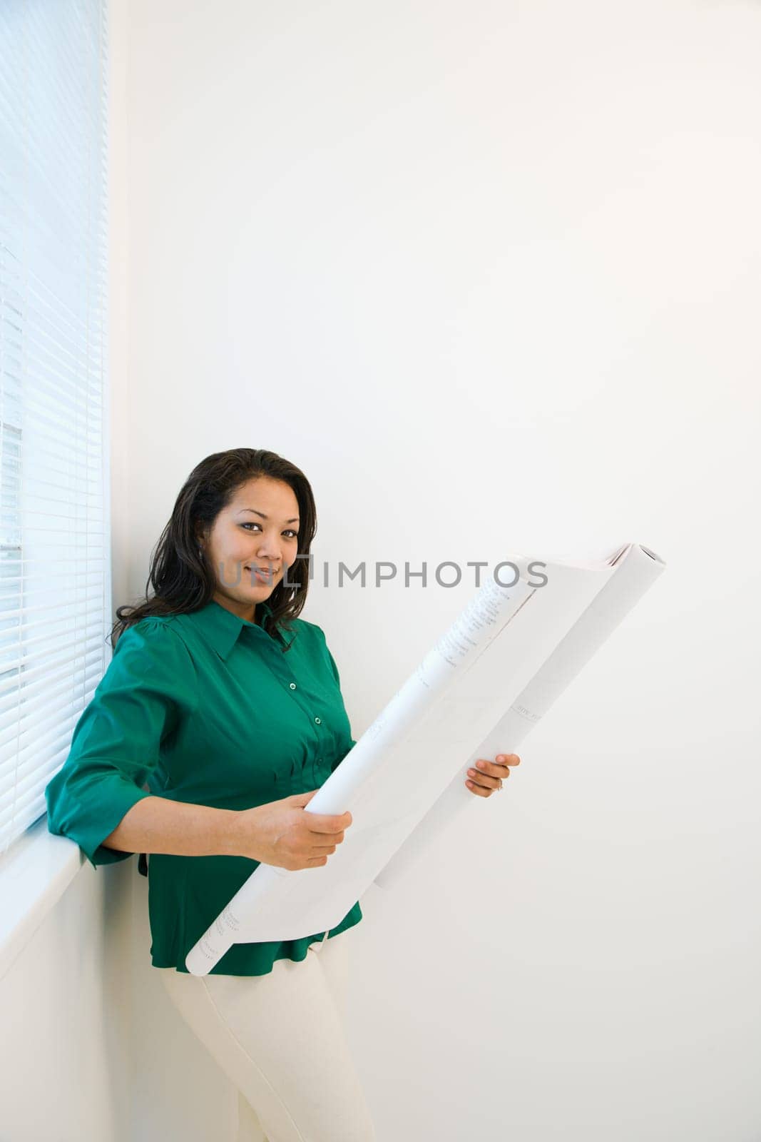 Businesswoman reading architectural blueprint plans and smiling.
