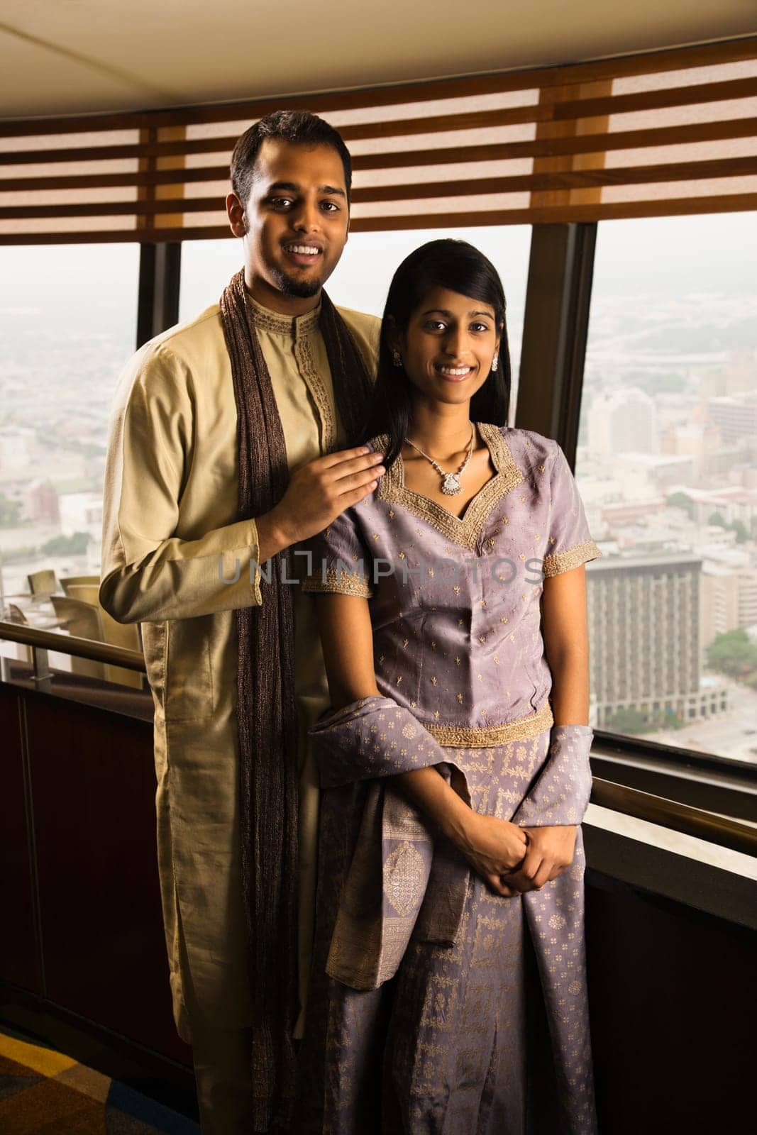 Portrait of a young adult couple standing near a high rise window and smiling at the camera. Vertical shot.