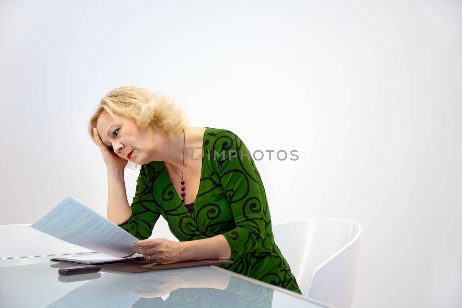 Caucasian middle aged businesswoman sitting at office desk reading paperwork.