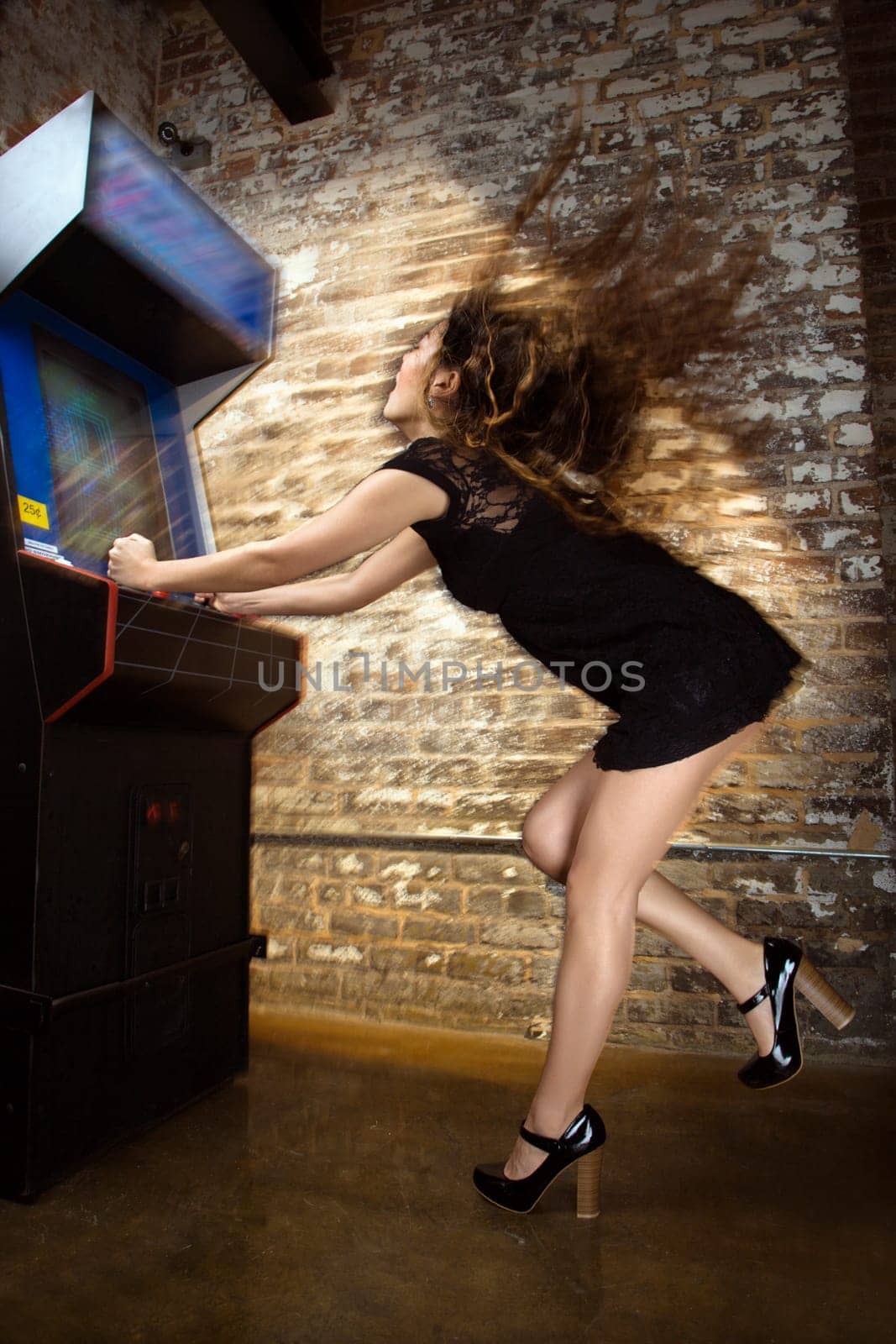 Attractive young woman standing wearing short dress playing video arcade game with hair flying out behind her.