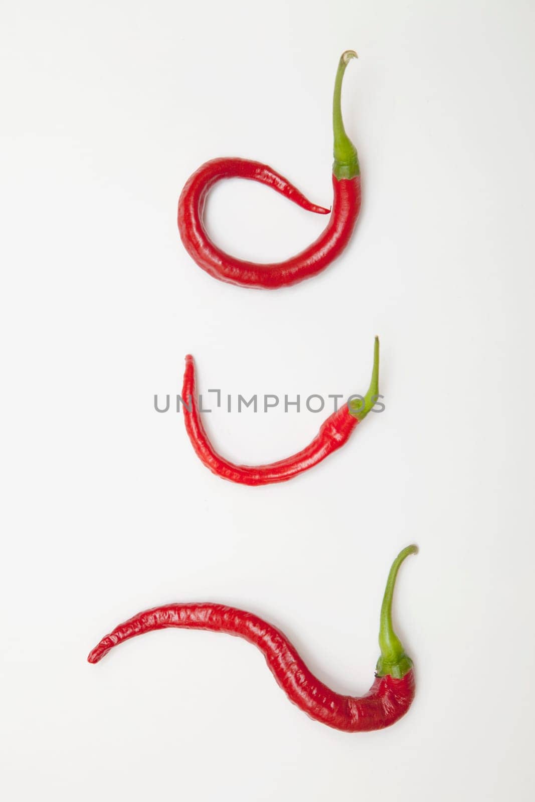 three red jalapeno peppers curled into unique shapes