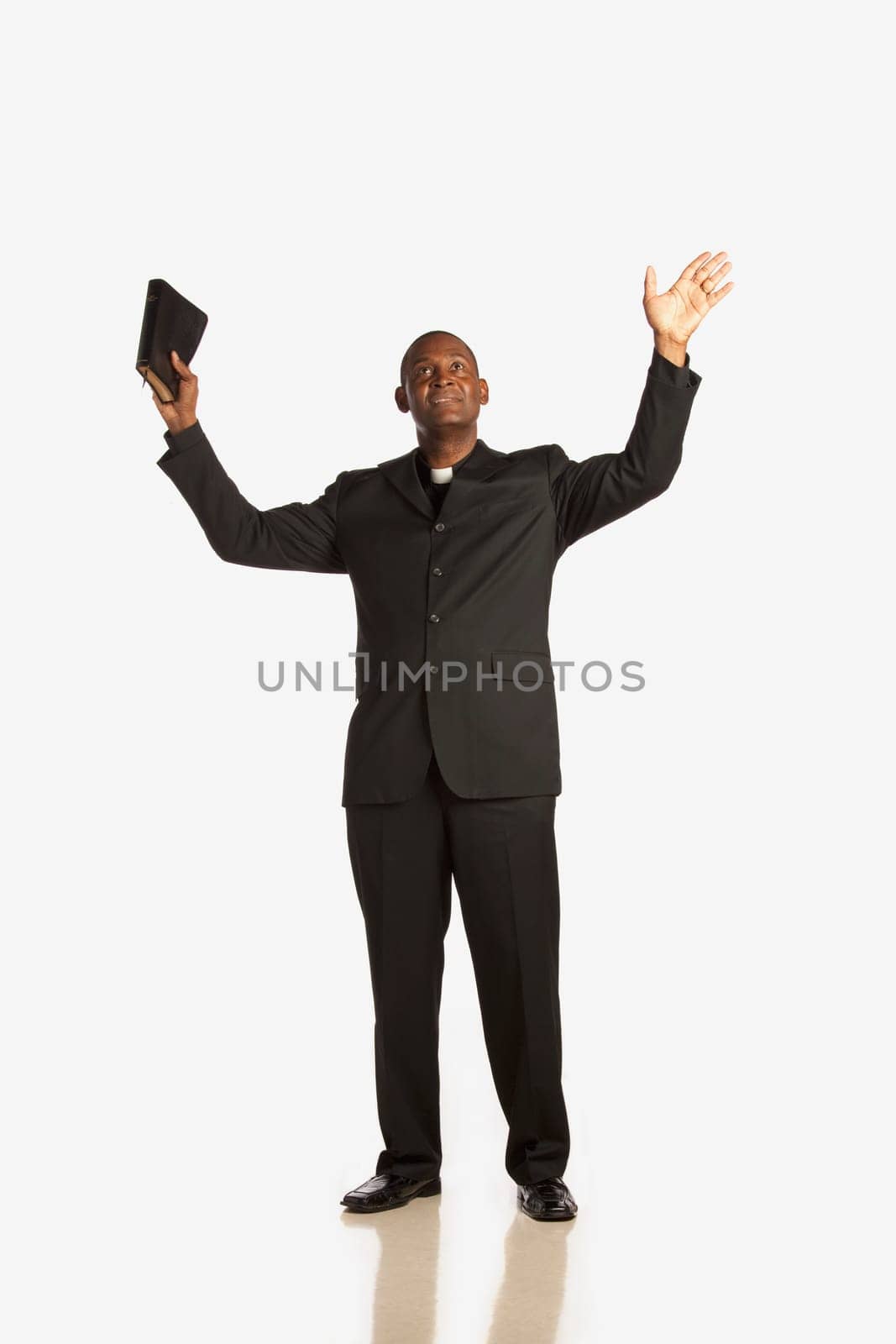 a man wearing a clerical collar and holding his bible up with hands raised and looking up
