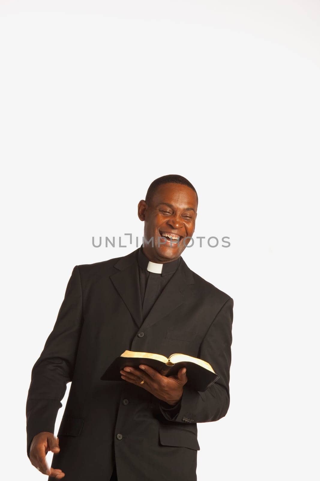 a man wearing a clerical collar and laughing while holding an open bible