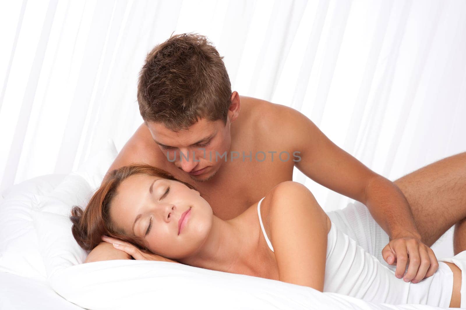 Young couple cuddle in bed on honeymoon