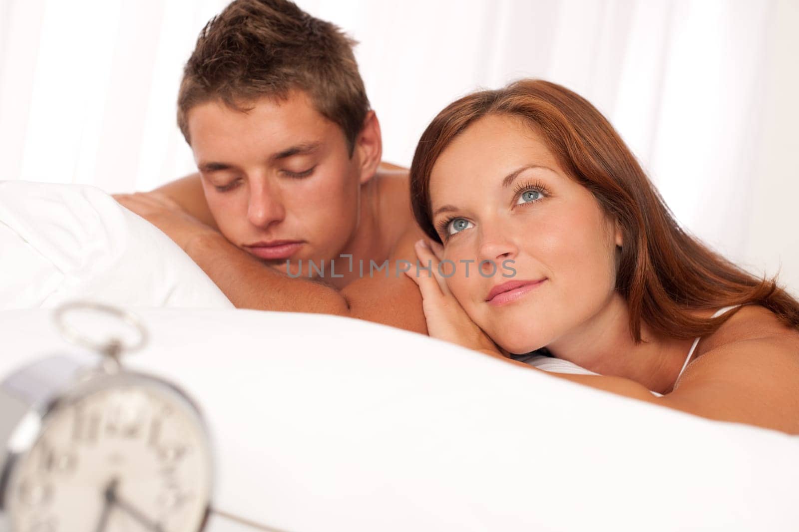 Young couple lying in white bed with alarm clock