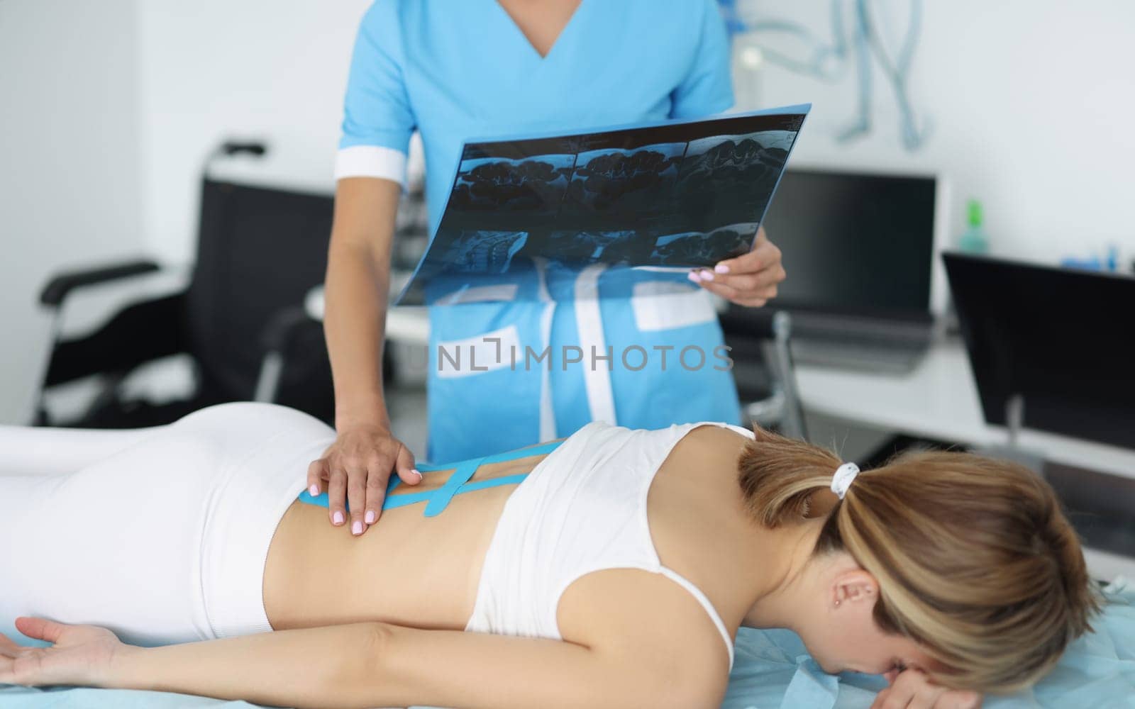 Doctor examine x ray of womans back, put kinesiology tape on ache part of body by kuprevich