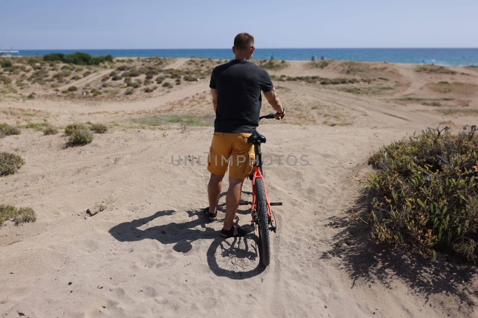 Portrait of person stand with back, arriving at his destination after bike ride to rest on beach. Nature, hobby, holiday, sport, physical activity concept