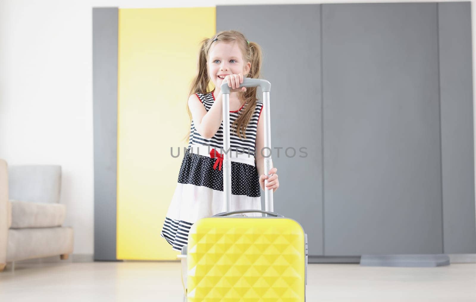 Portrait of pretty little girl going on vacation, packed stuff in yellow suitcase, kid in lovely summer dress. Childhood, tourism, dream, toddler concept