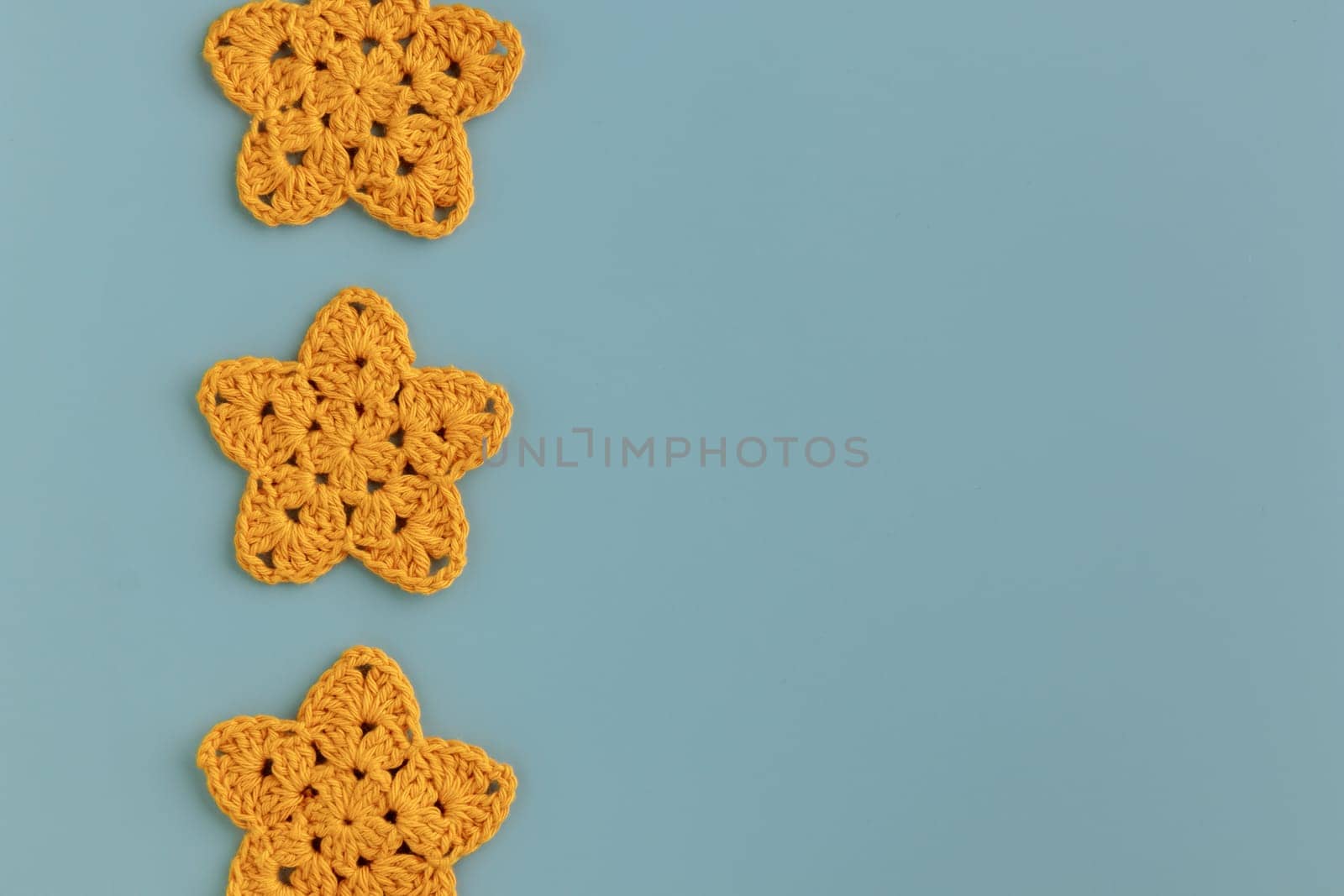 Three yellow crocheted stars row pattern on a blue background