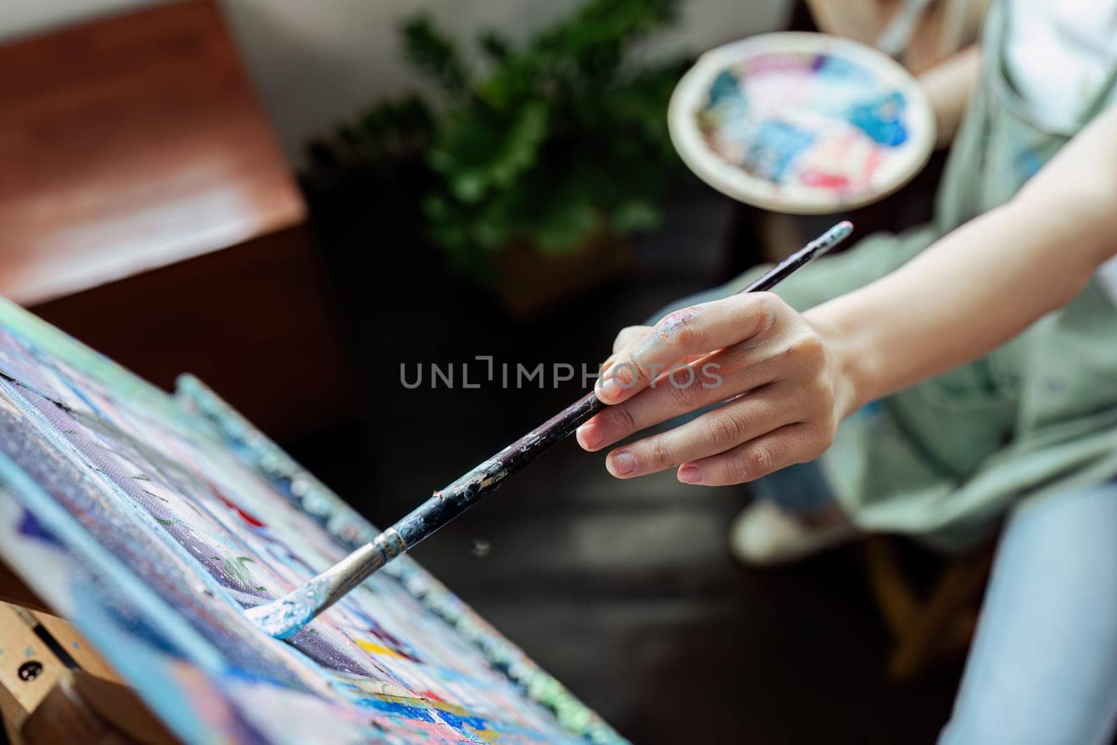 Female artist hold color palette and paintbrush for painting during hobby workshop.