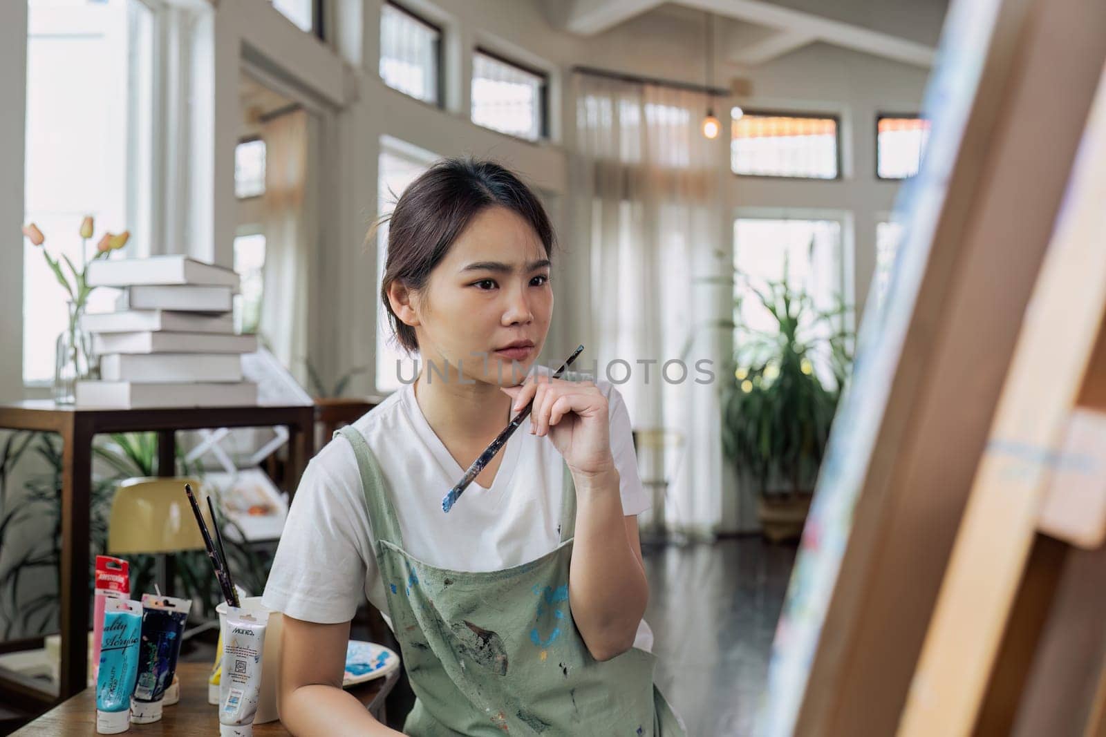 Female artist thinking and hold paintbrush while looking at canvas and pondering about paintin by itchaznong