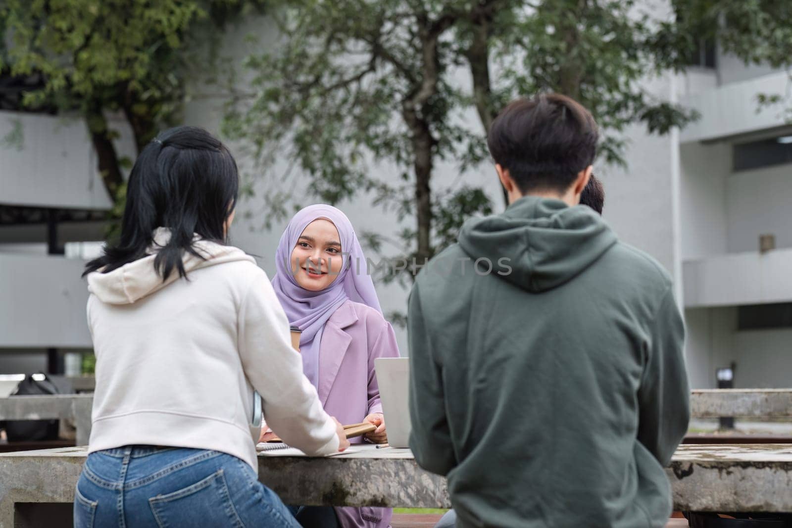 A multiracial group of students at the college, including Muslim and Asian students, sat on benches in a campus break area. Read books or study for exams together. by wichayada