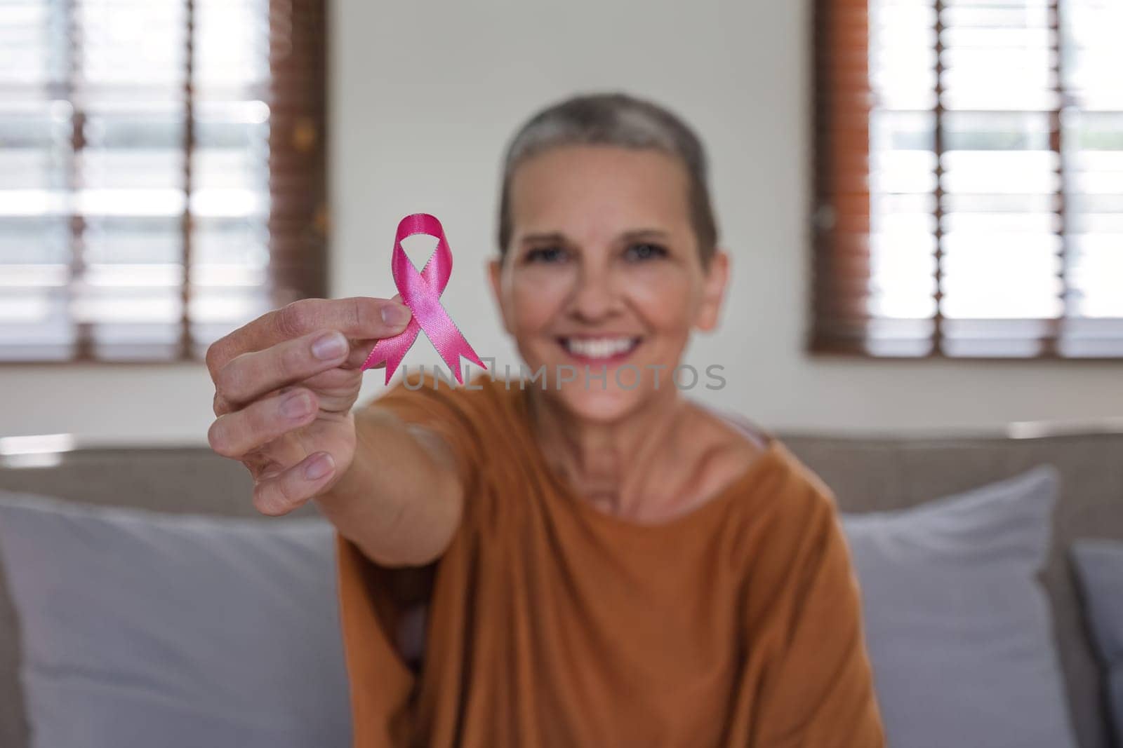 Portrait of confident smiling elderly senior woman with pink ribbon at her home. Health care, support, prevention. Breast cancer awareness month concept by wichayada