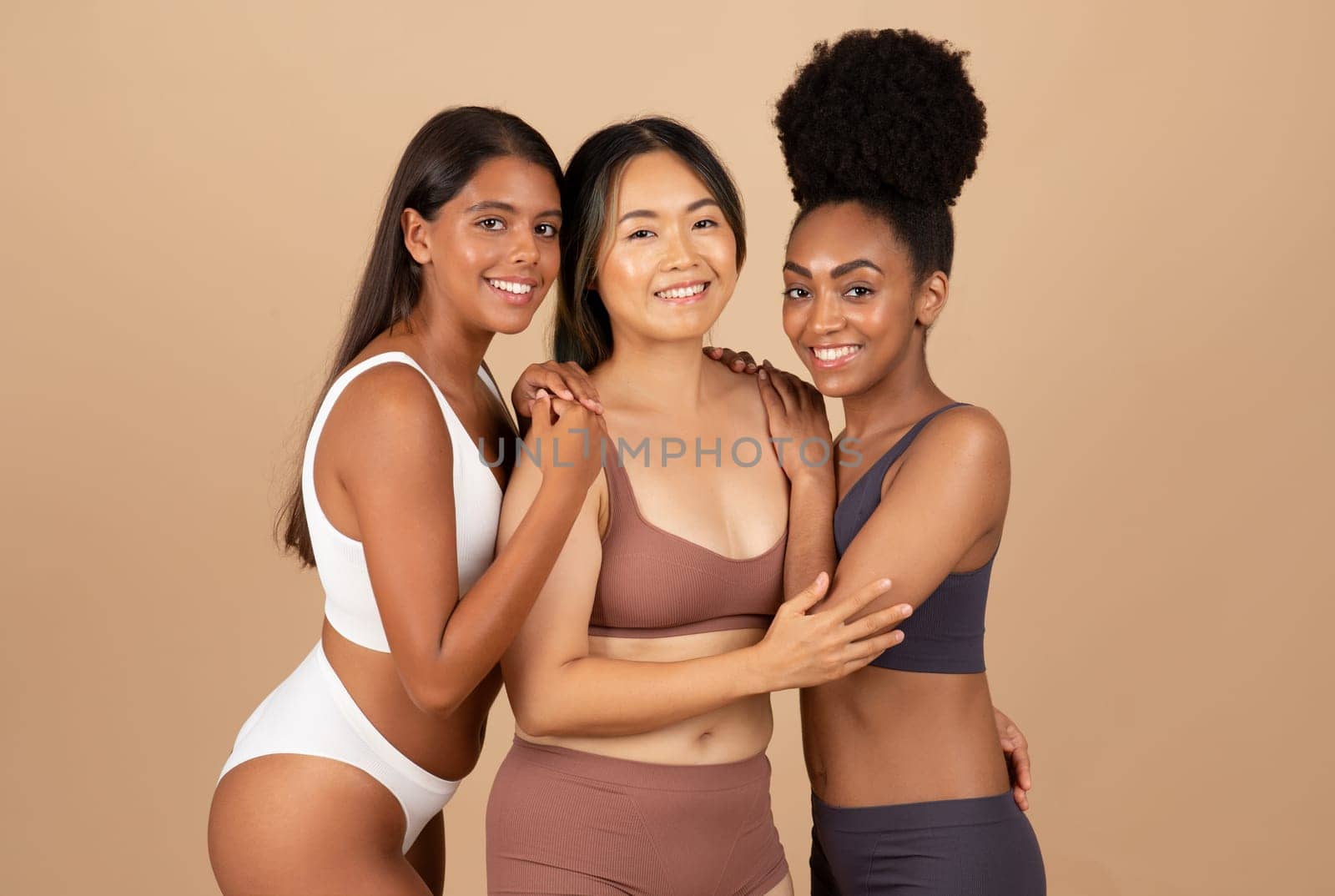 Three multiracial women exude natural beauty while posing in underwear, offering refreshing, authentic and harmonious image on beige studio background