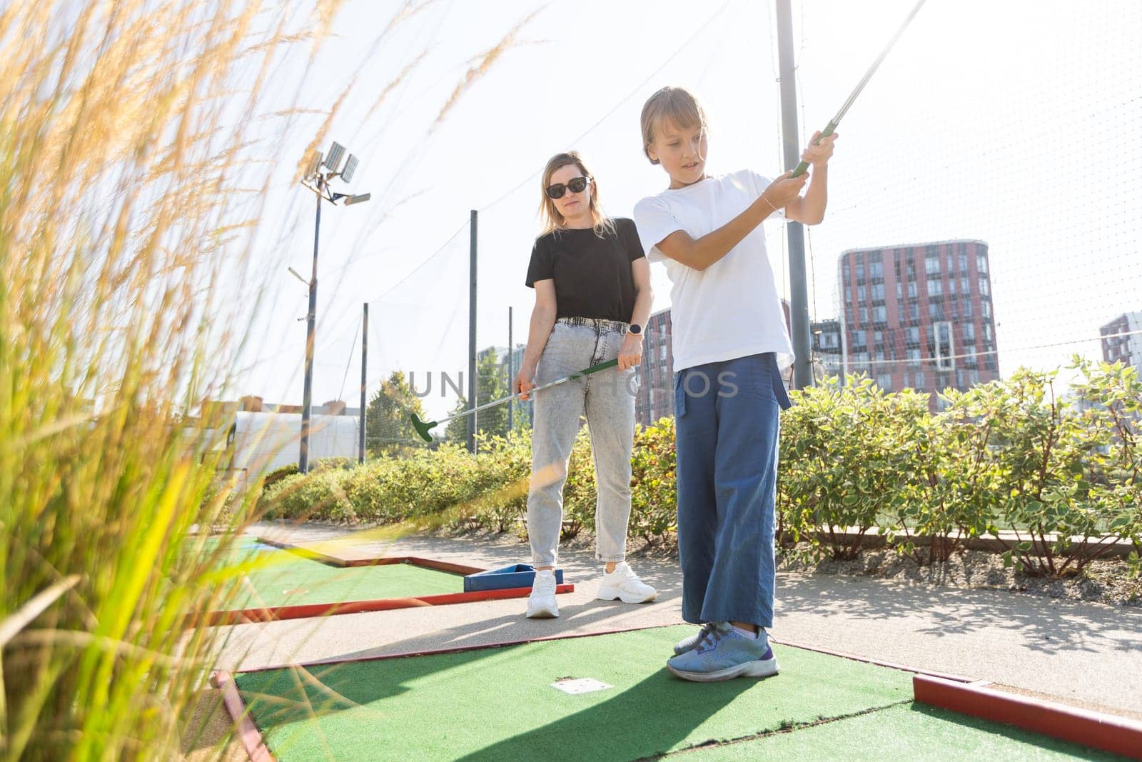 Cute school girl playing mini golf with family. Happy toddler child having fun with outdoor activity. Summer sport for children and adults, outdoors. Family vacations or resort. High quality photo