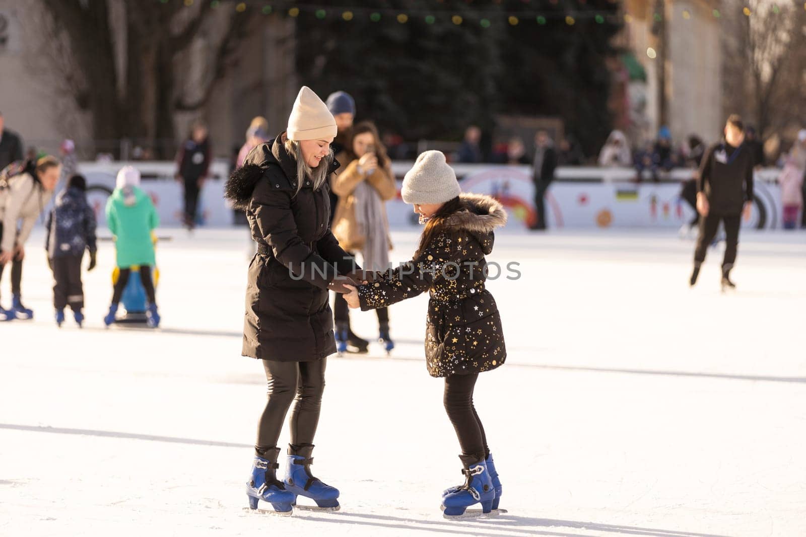 Action shot of beautiful woman teaching her daughter how to ice skate by Andelov13